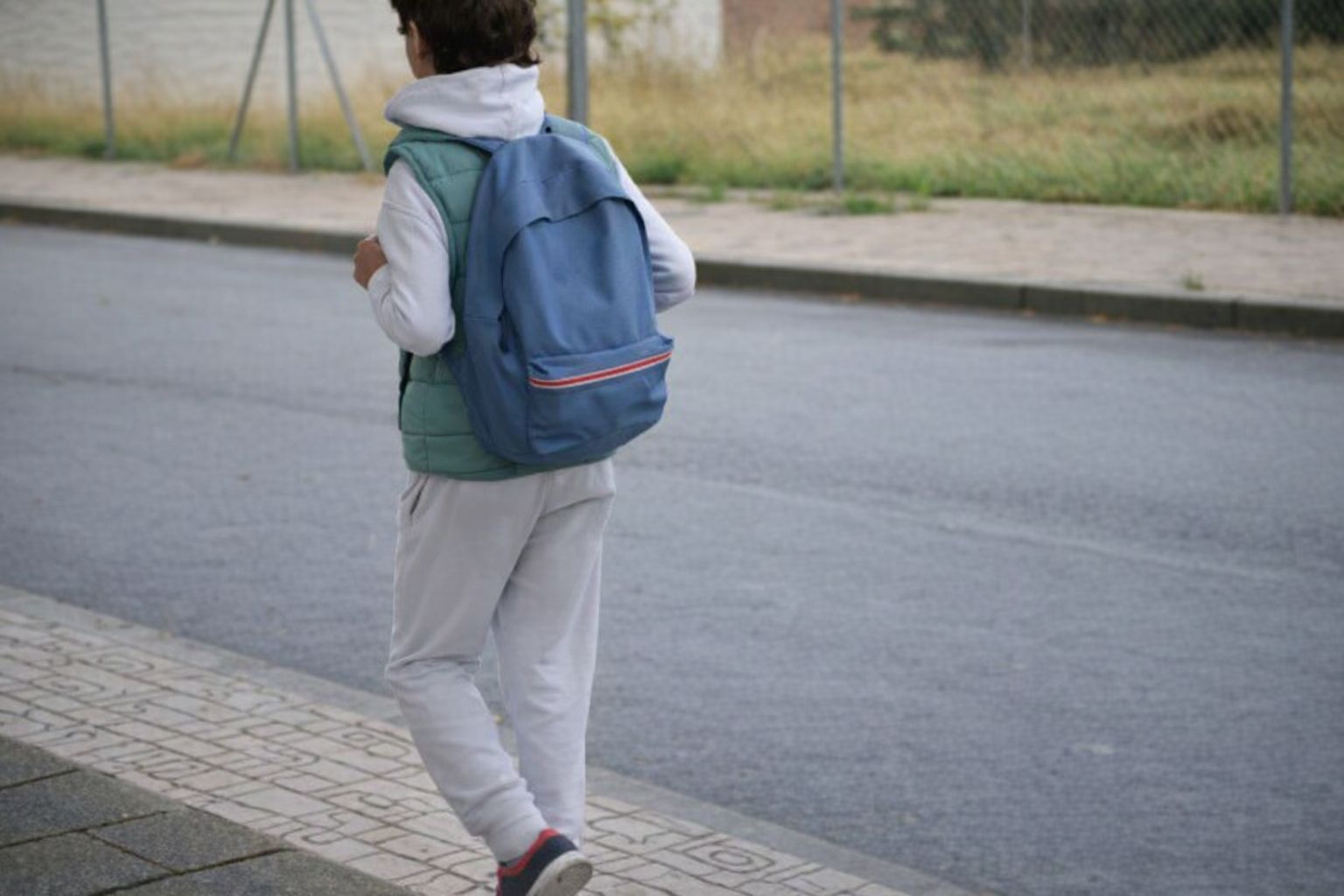 Barn sedd bakifrån i vit hoodie och blå ryggsäck på väg till skolan.