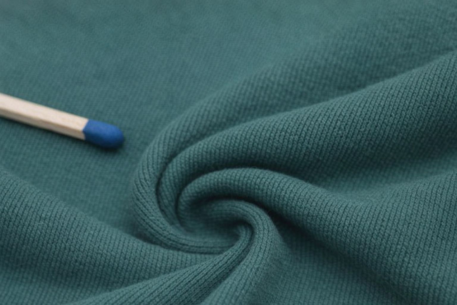 Närbild på grönt hoodie-tyg med en tändsticka som storleksreferens.