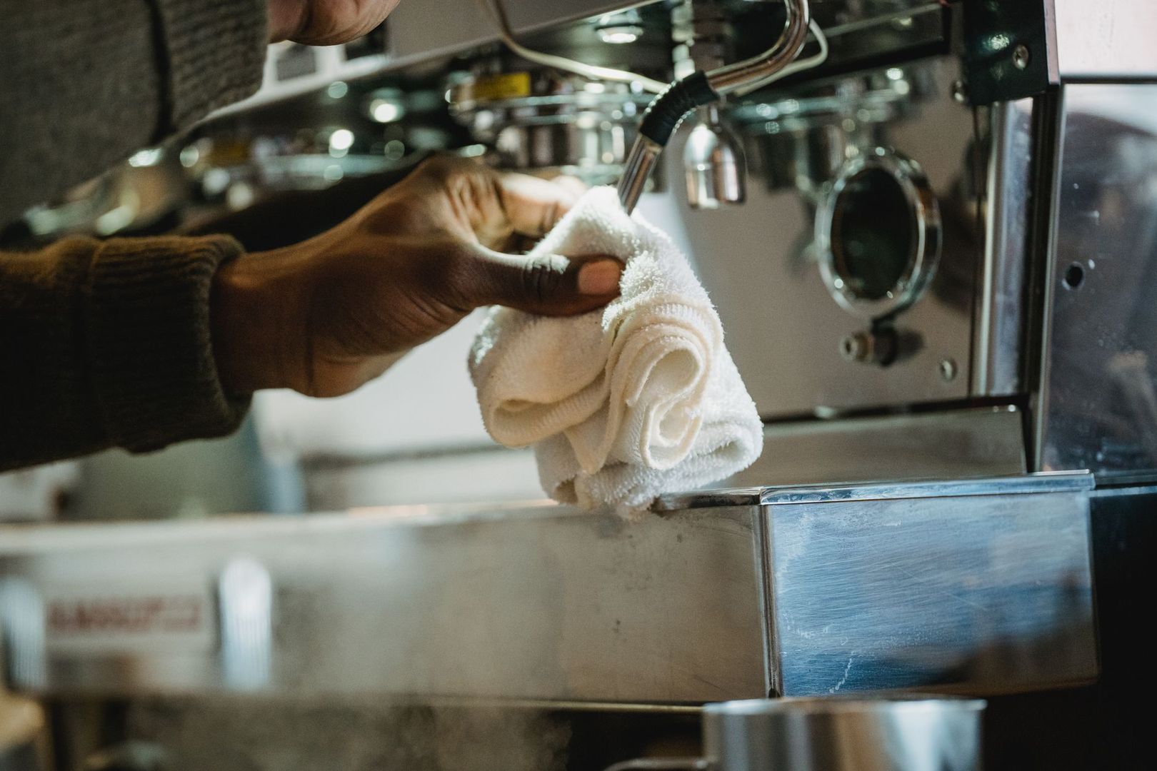 En barista rengör ångrör på en espressomaskin med en trasa.