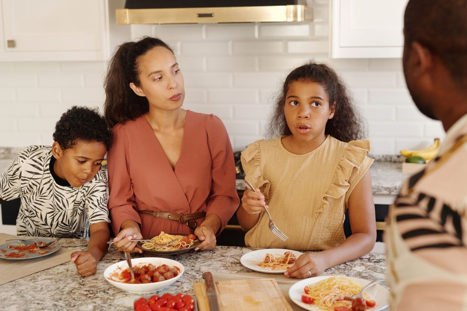Familj samlas kring köksön med tallrikar pasta och köttbullar